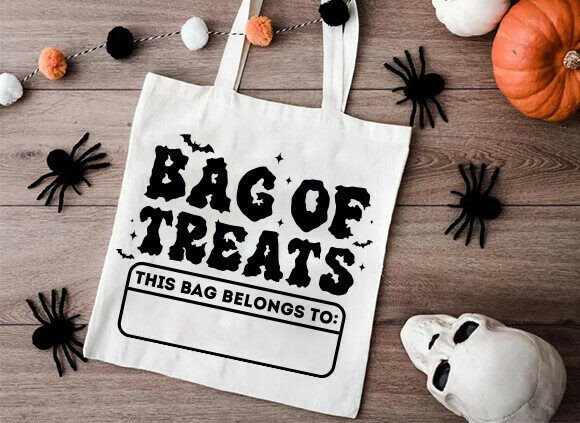Tote bag with 'Bag of Treats' text on a wooden surface with Halloween decorations.