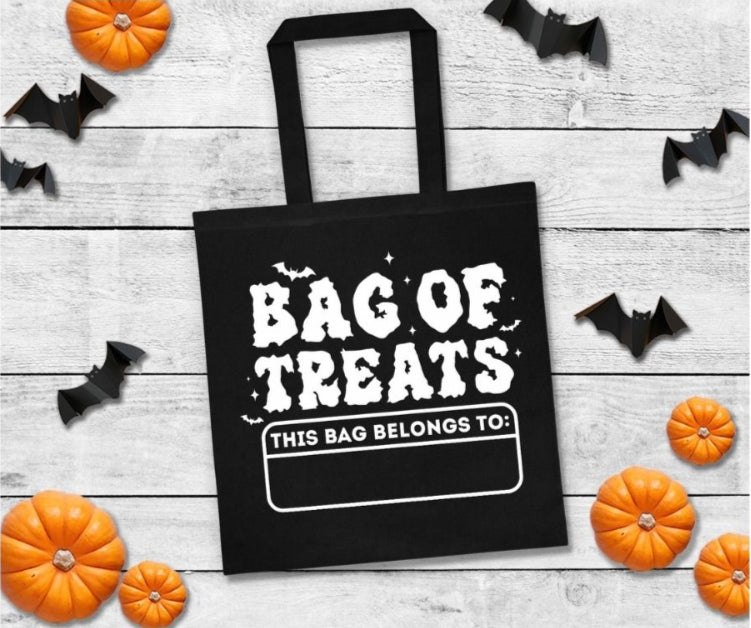 Black tote bag with 'Bag of Treats' text on a wooden surface with Halloween decorations.